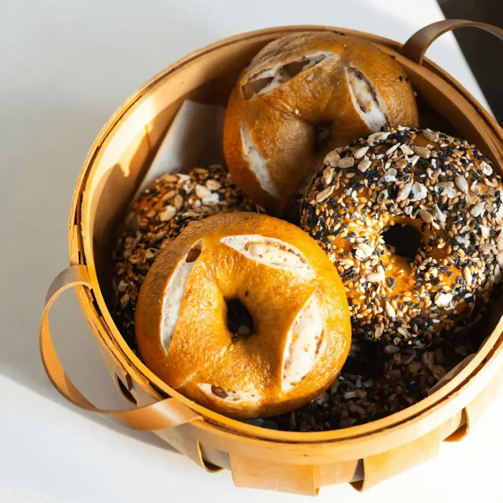 A freshly baked protein bagel with a golden-brown crust, sliced open to reveal a soft, chewy texture, served on a wooden board with cream cheese and fresh berries.